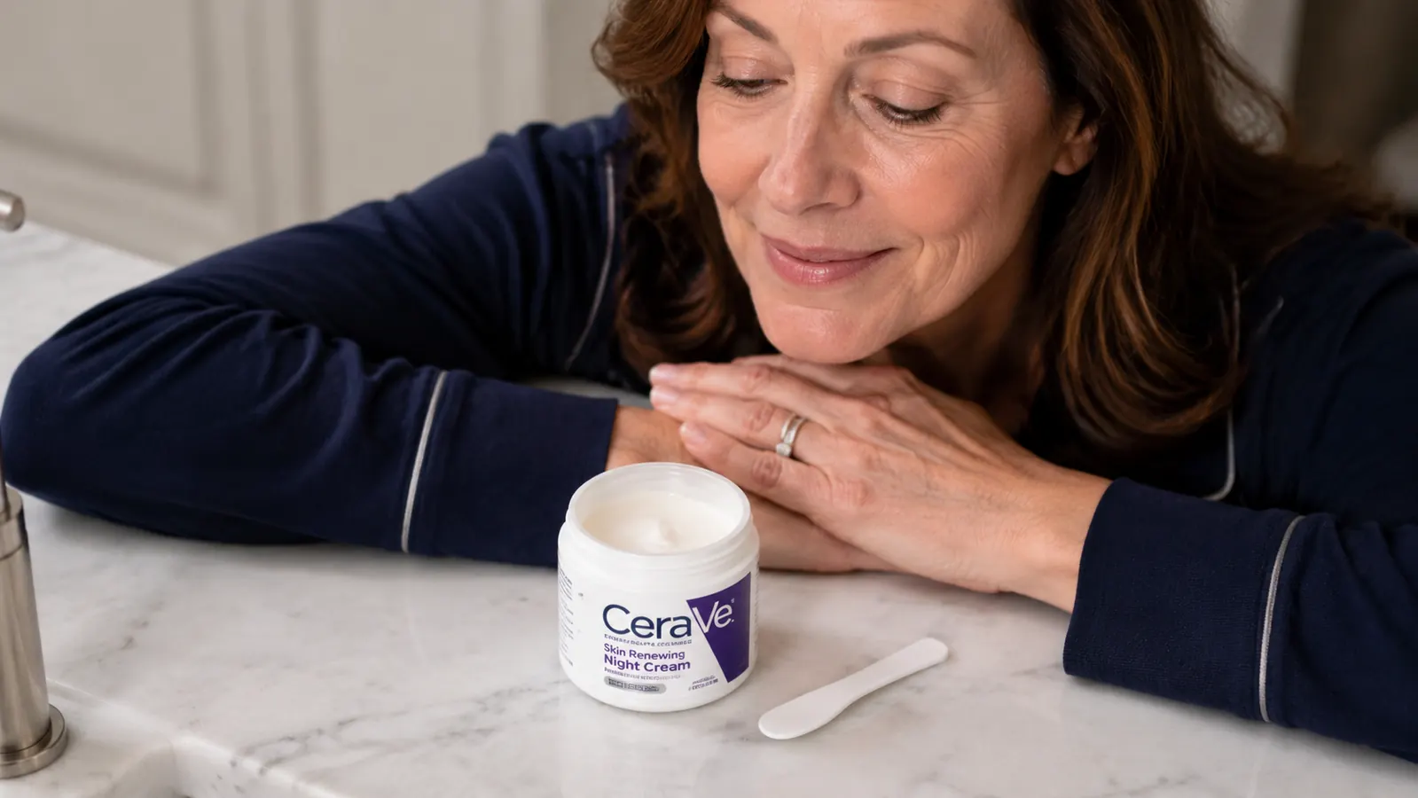 CeraVe Skin Renewing Night Cream jar open on a marble bathroom counter with a soft towel beside it