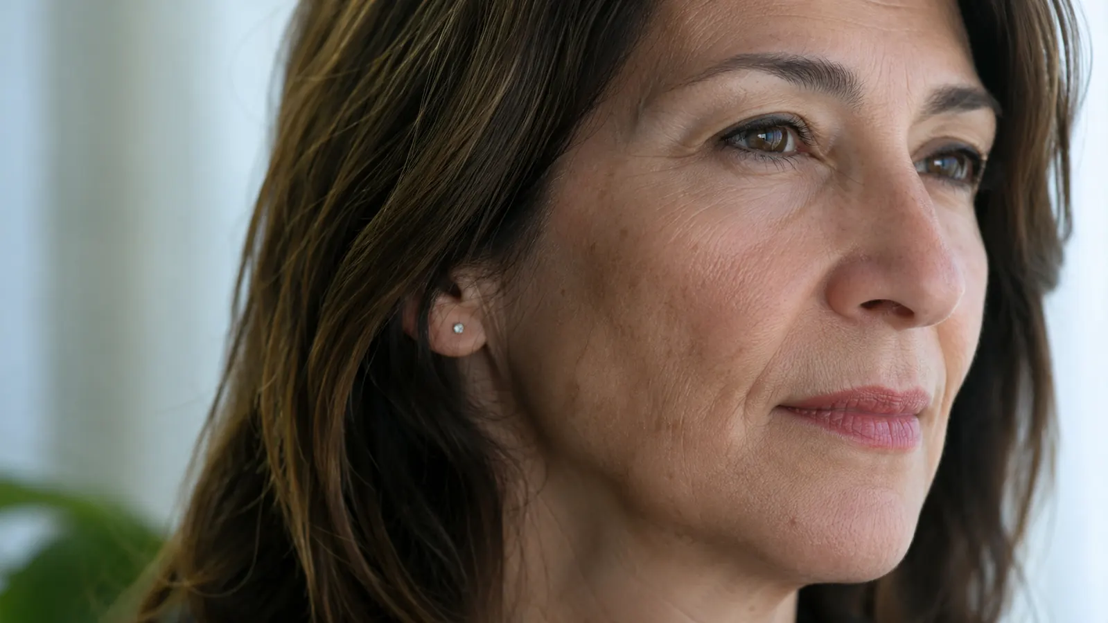 Close-up of woman's cheek and jawline showing skin texture with faint dark spots in natural light